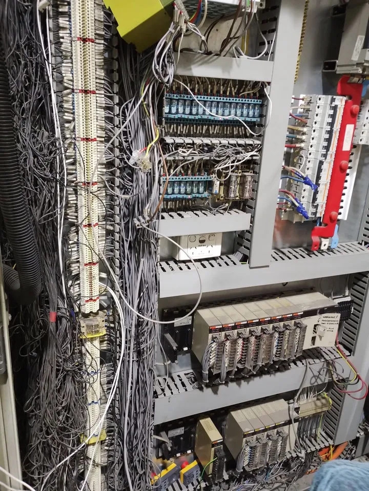 Original switchboard packed with relay banks, contactors, legacy PLC racks and dense point-to-point wiring looms